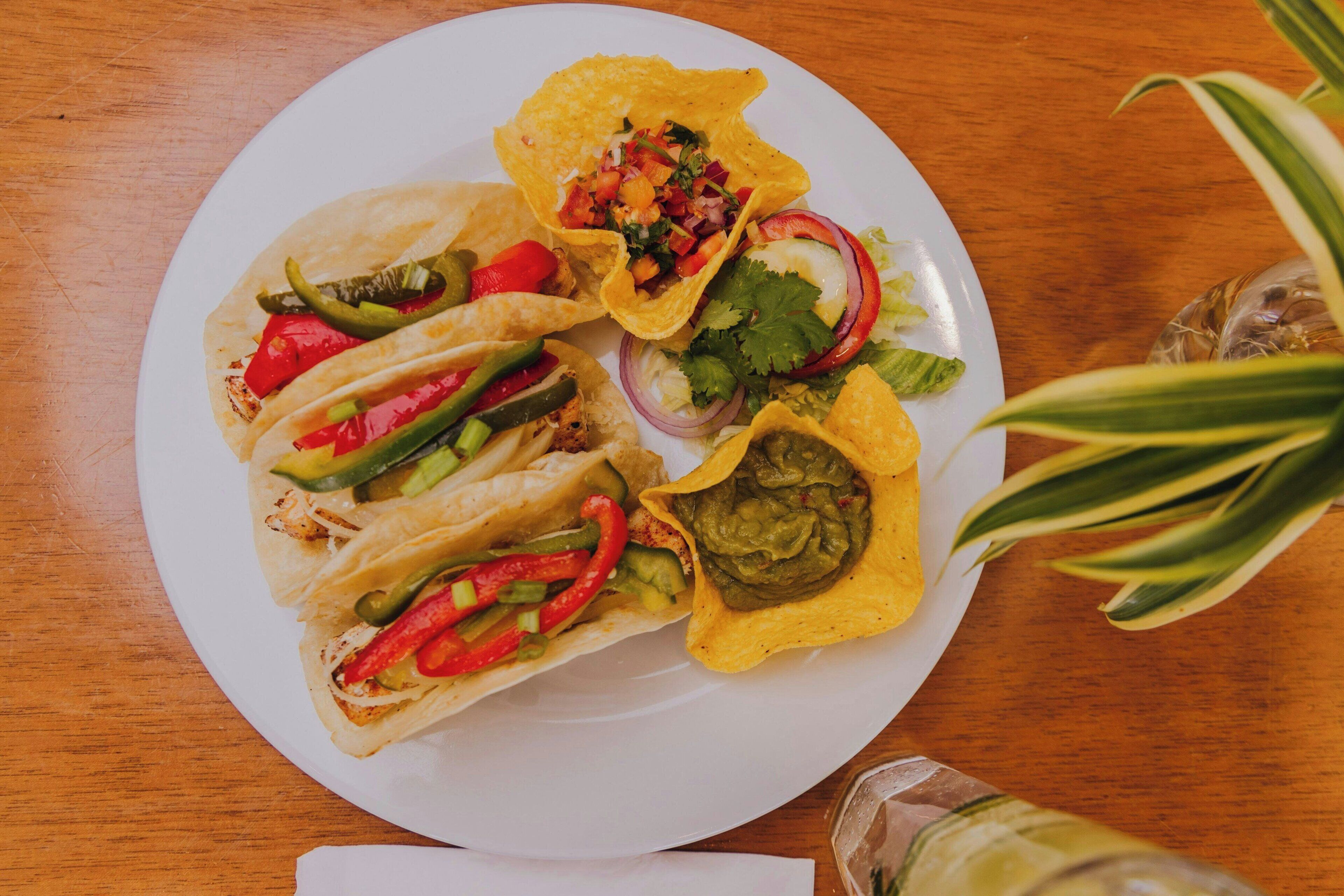 A plate of tacos with various toppings and a side salad on a wooden table.