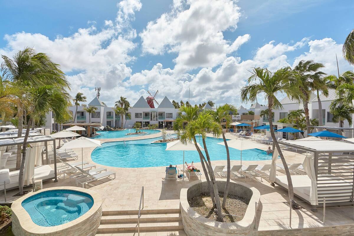 Un resort con una amplia piscina central, varias piscinas más pequeñas y zonas de descanso con sombrillas.
