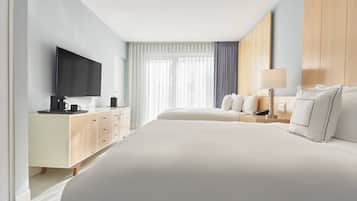 Une chambre d’hôtel avec un grand lit, un téléviseur fixé au mur, une table de chevet avec une lampe et une fenêtre avec des rideaux légers.