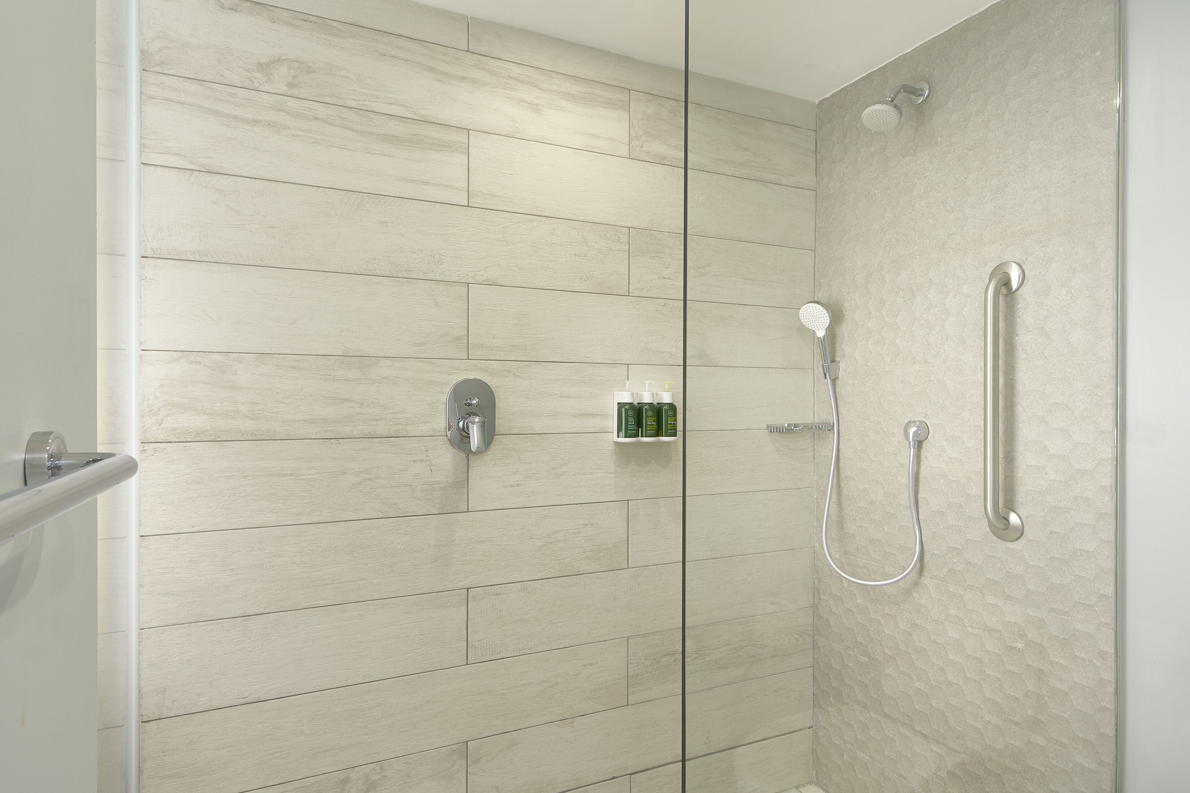 A modern shower area with a glass door, a handheld showerhead, and a wall-mounted faucet.