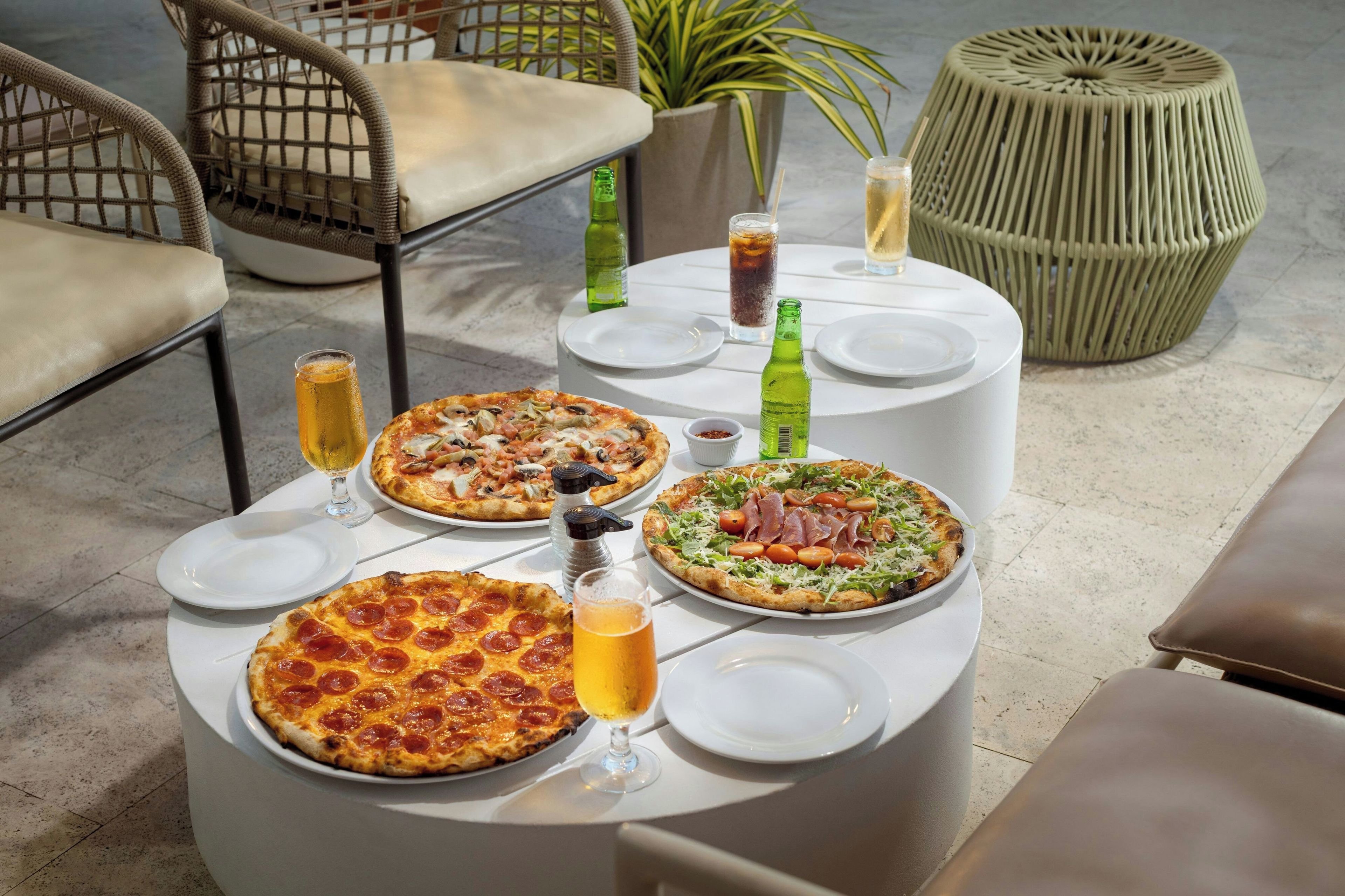 A table with four pizzas, two glasses of beer, and two bottles of soda.