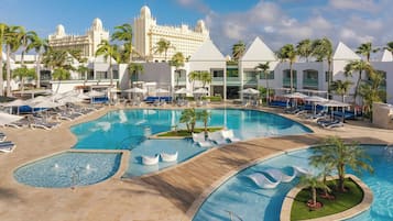 Un resort con varias piscinas, palmeras y un edificio grande al fondo.