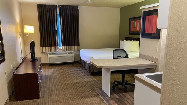 A hotel room with a bed, desk, chair, and a small kitchenette.