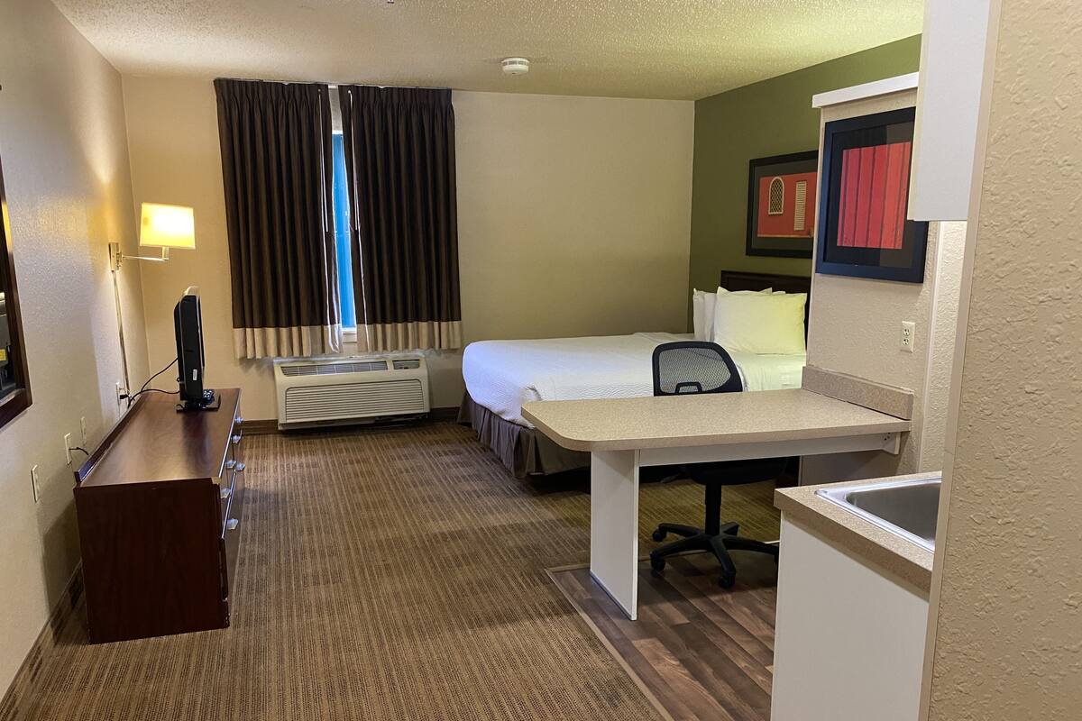 Une chambre d’hôtel équipée d’un lit, d’un bureau, d’une chaise et d’une petite kitchenette.