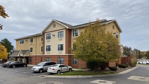 A multi-story hotel with a beige and brown facade, multiple windows, and a parking lot with several cars.