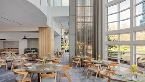 Un comedor amplio con varias mesas y sillas, ventanas grandes que ofrecen vistas al exterior, y un diseño arquitectónico moderno con techo alto y luz natural.