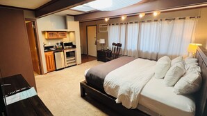 A hotel room with a large bed, a desk with a computer, a kitchenette, and a bathroom.