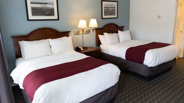 A hotel room with two beds, a nightstand with a lamp, and framed pictures on the wall.