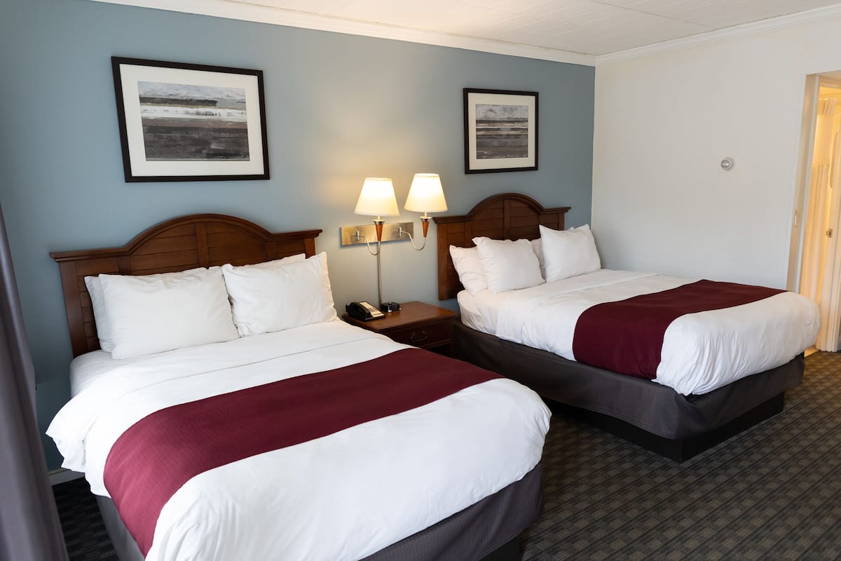A hotel room with two beds, a nightstand with a lamp, and framed pictures on the wall.