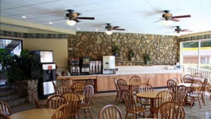 A restaurant with stone walls, wooden tables and chairs, ceiling fans, and a counter with a coffee machine.