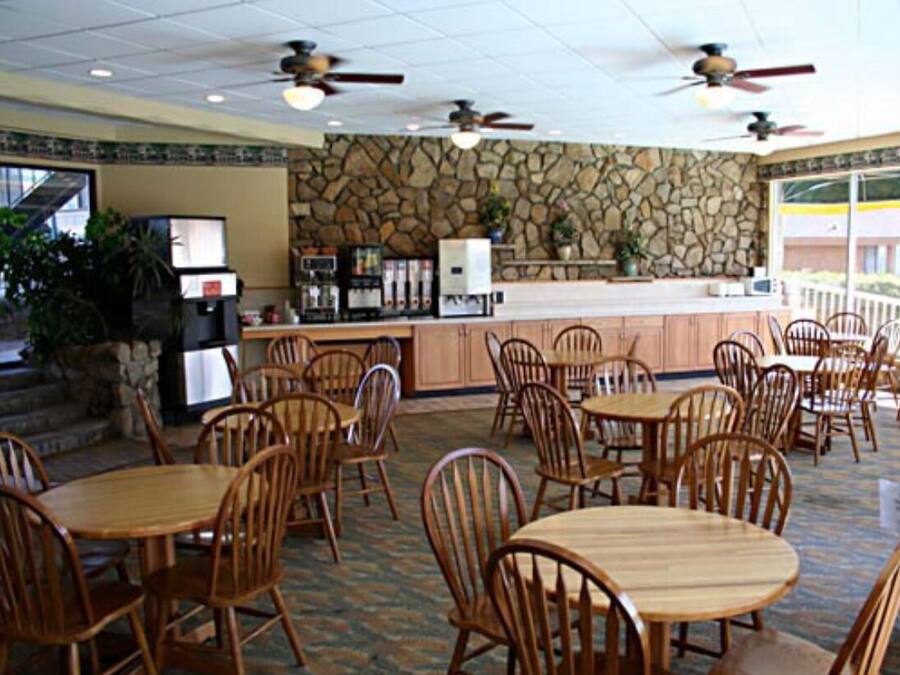 Un restaurante con paredes de piedra, mesas y sillas de madera, ventiladores de techo y una barra con una máquina de café.