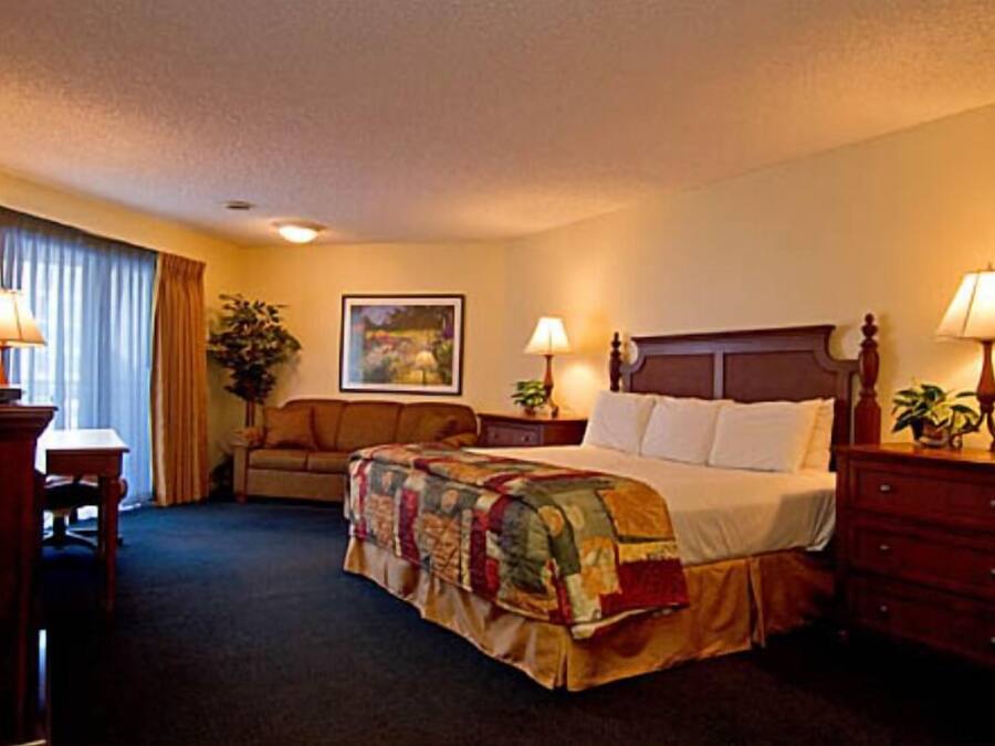 A hotel room with a bed, a desk, a chair, a sofa, and a nightstand with lamps.