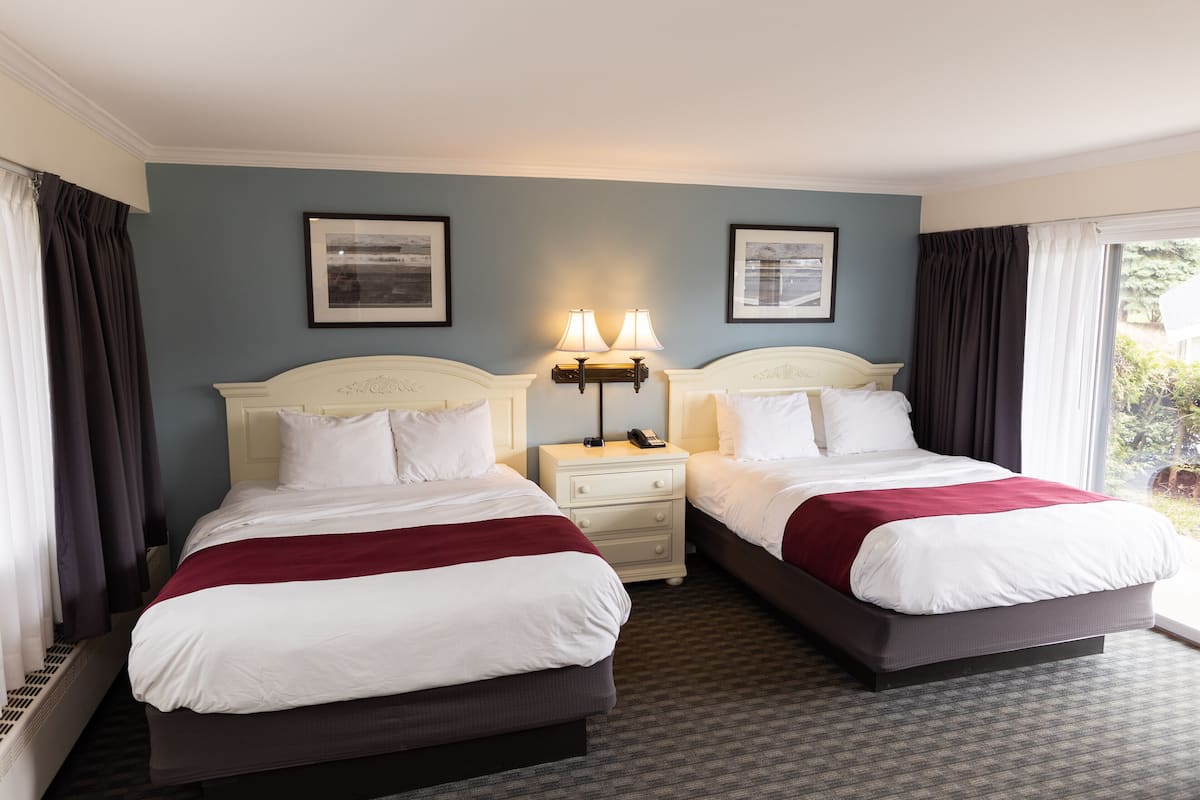 A hotel room with two beds, a nightstand with lamps, and framed pictures on the wall.