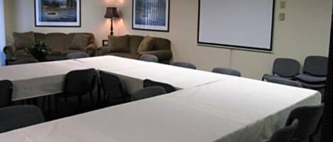 A conference room with a long table, several chairs, a projector screen, and two framed pictures on the wall.