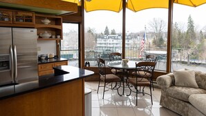 A modern kitchen with a stainless steel refrigerator, wooden cabinets, and a large window overlooking a balcony with outdoor furniture.