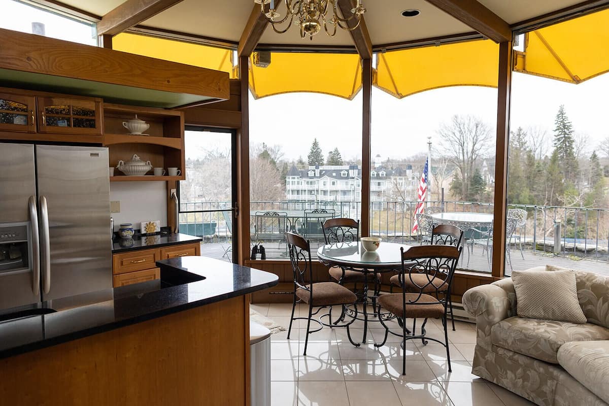 A modern kitchen with a stainless steel refrigerator, wooden cabinets, and a large window overlooking a balcony with outdoor furniture.