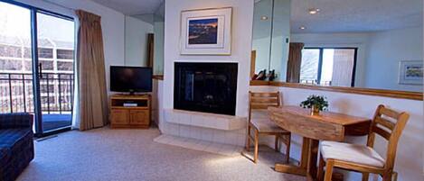 Una sala de estar con chimenea, televisor, mesa de comedor con sillas y un espejo grande.