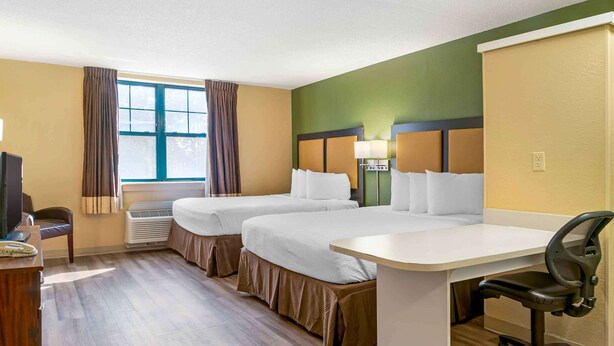 Habitación de hotel con dos camas, un escritorio, una silla y un televisor.