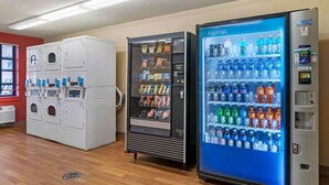 Una habitación de hotel con lavadora, máquina expendedora de aperitivos y dispensador de agua.