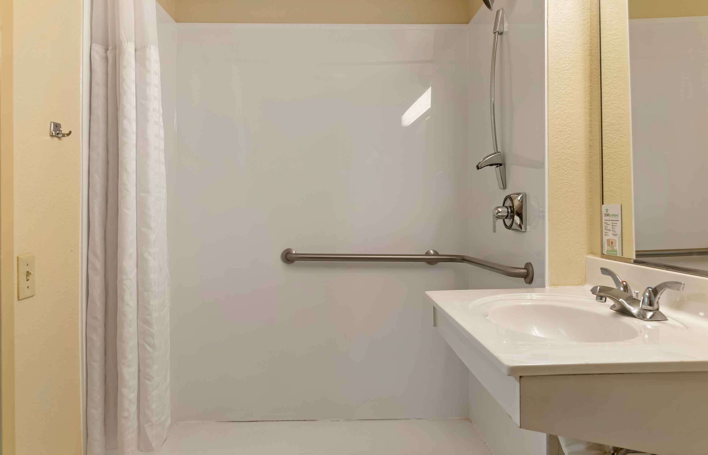 A bathroom with a shower, a handrail, a sink, and a mirror.