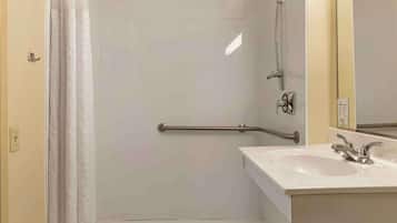 A bathroom with a shower, a handrail, a sink, and a mirror.