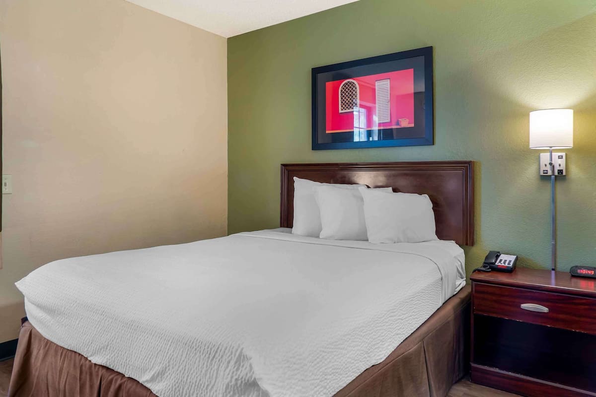 Una habitación de hotel con una cama grande, una mesita de noche con teléfono, una lámpara de pared y un cuadro enmarcado sobre la cama.
