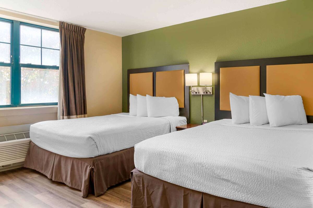 Habitación de hotel con dos camas, un ventanal con cortinas, una lámpara de pared y un calentador.