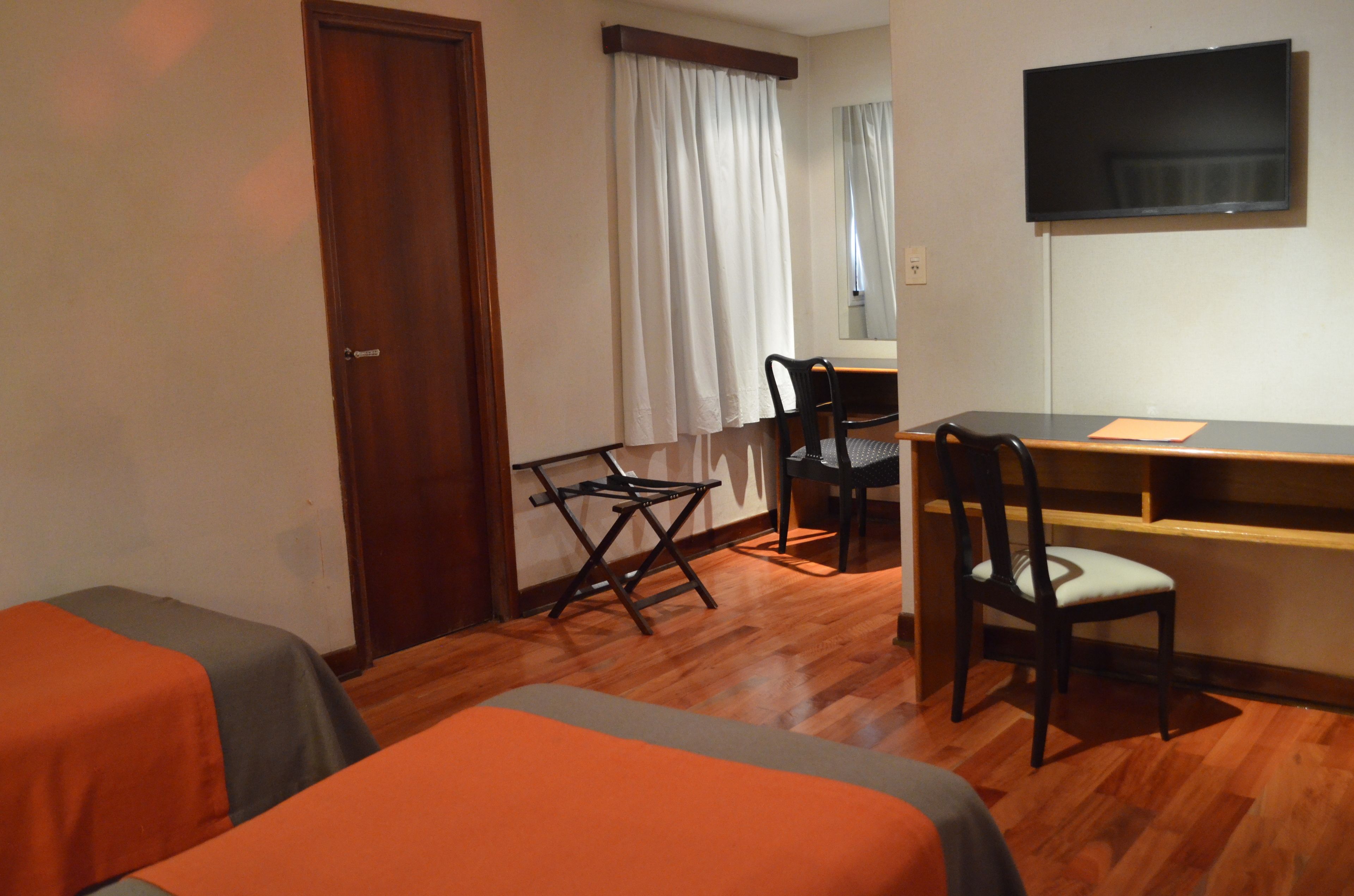 A hotel room with two beds, a desk, a chair, a television, and a window with curtains.
