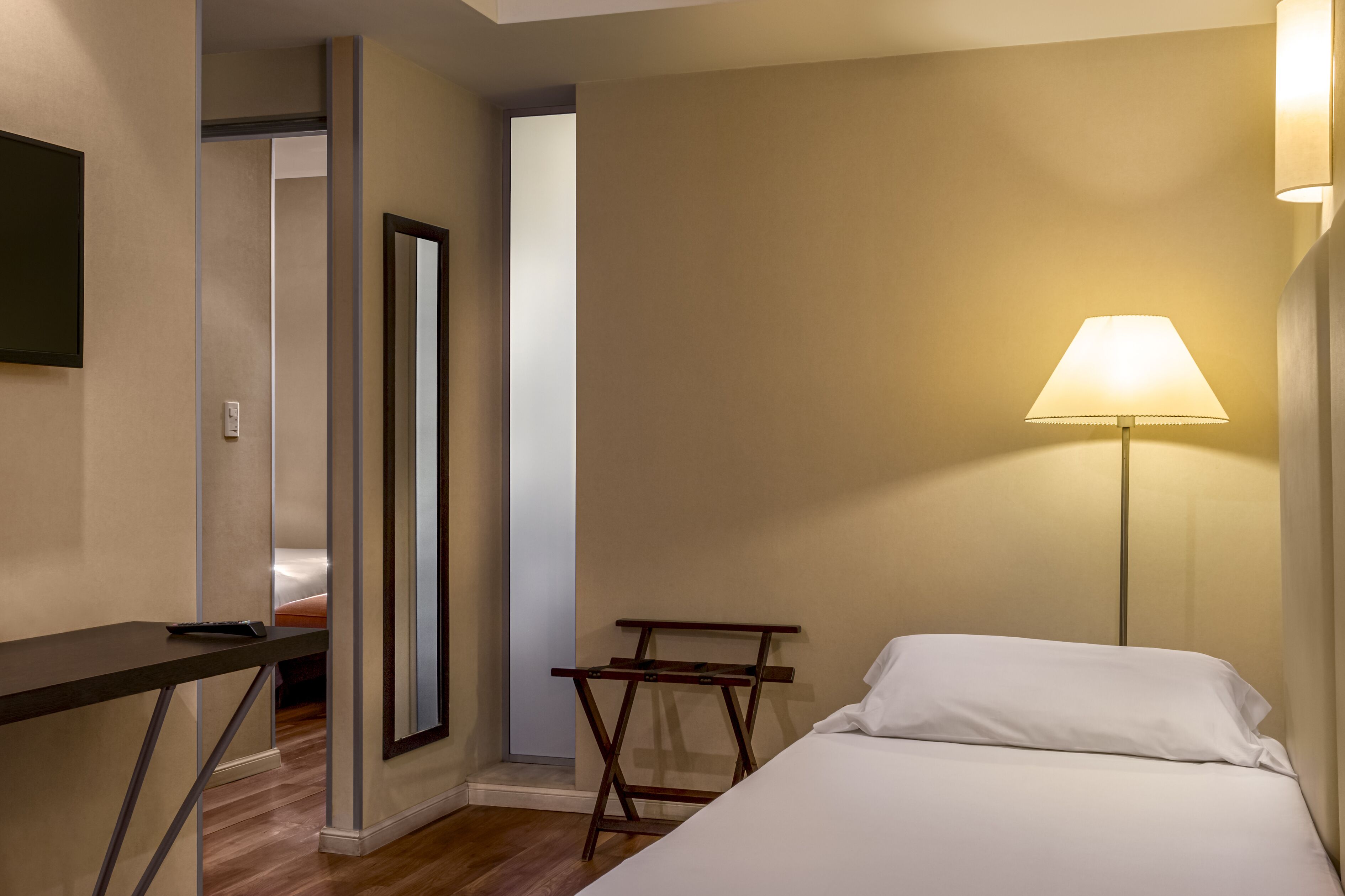 A hotel room with a bed, a desk, a lamp, and a mirror.