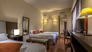 Habitación de hotel con dos camas, un escritorio, una silla y una lámpara.