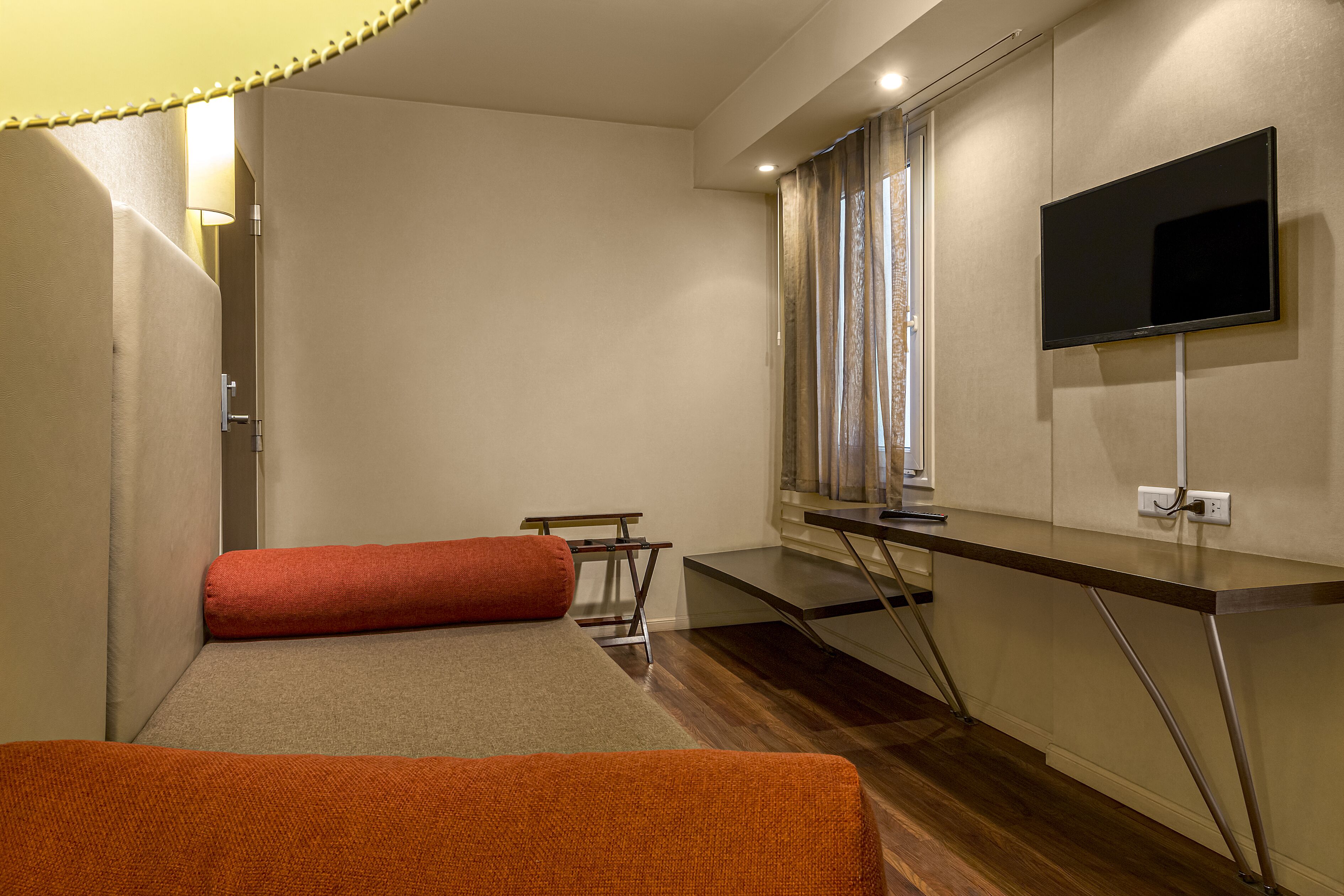 Una camera d'hotel con un letto, una scrivania, una TV e una finestra con tende.