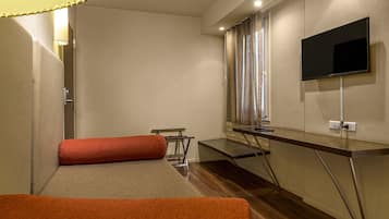 Habitación de hotel con cama, escritorio, televisión y ventana con cortinas.