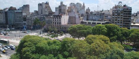 Un paisaje urbano con una mezcla de edificios modernos y antiguos, una rotonda en el centro y abundante vegetación en primer plano.