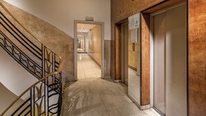 Un vestíbulo de hotel con una escalera de mármol, un ascensor y un pasillo que conduce a otras áreas.