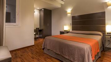 A hotel room with a large bed, a bedside table with a lamp, a wardrobe, and a chair.