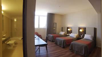Habitación de hotel con dos camas, ducha, lavamanos y una mesa.