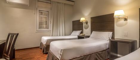 A hotel room with two beds, a desk, a chair, and a window with curtains.