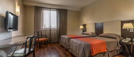 Habitación de hotel con dos camas, un escritorio, una silla, un televisor y una ventana con cortinas.