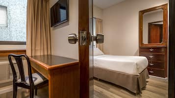 Habitación de hotel con escritorio de madera, cama, cómoda y televisor en la pared.