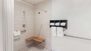 A shower area with a bench, a towel rack, and a shelf with folded towels. - Howard Johnson by Wyndham National City/San Diego South (National City)