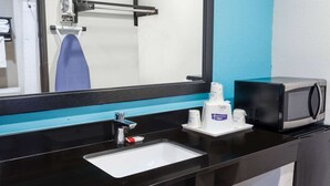 A hotel bathroom with a black sink, a mirror, a towel rack, a microwave, and toiletries on the counter. - Howard Johnson by Wyndham National City/San Diego South (National City)