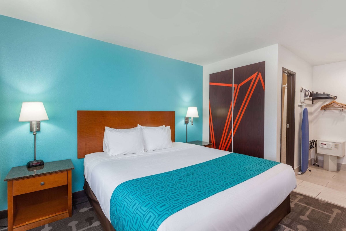 Une chambre d’hôtel avec un grand lit, deux lampes de chevet, une table de chevet en bois, un mur bleu et une armoire au motif géométrique.