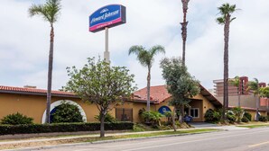 A Howard Johnson Express Inn with a prominent sign, palm trees, and a building with a red-tiled roof. - Howard Johnson by Wyndham National City/San Diego South (National City)