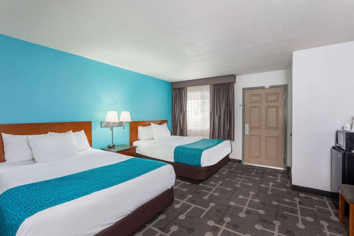 Une chambre d’hôtel avec deux lits, un bureau, une chaise, une télévision et une porte.