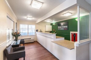 Un área de recepción con una pared verde, mostrador de recepción, teléfono, ventana y una silla.