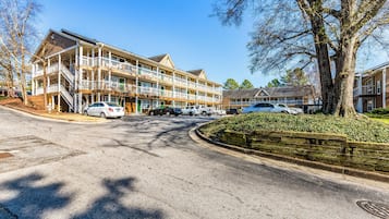 A multi-story hotel with balconies, a parking lot, and a tree-lined street.