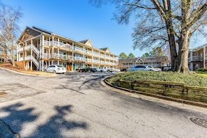 A multi-story hotel with balconies, a parking lot, and a tree-lined street. - HomeTowne Studios by Red Roof Atlanta - Norcross Downtown (Norcross)