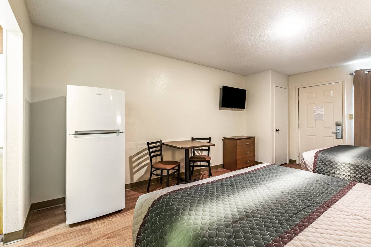 A hotel room with a bed, a desk, a chair, a refrigerator, and a television.