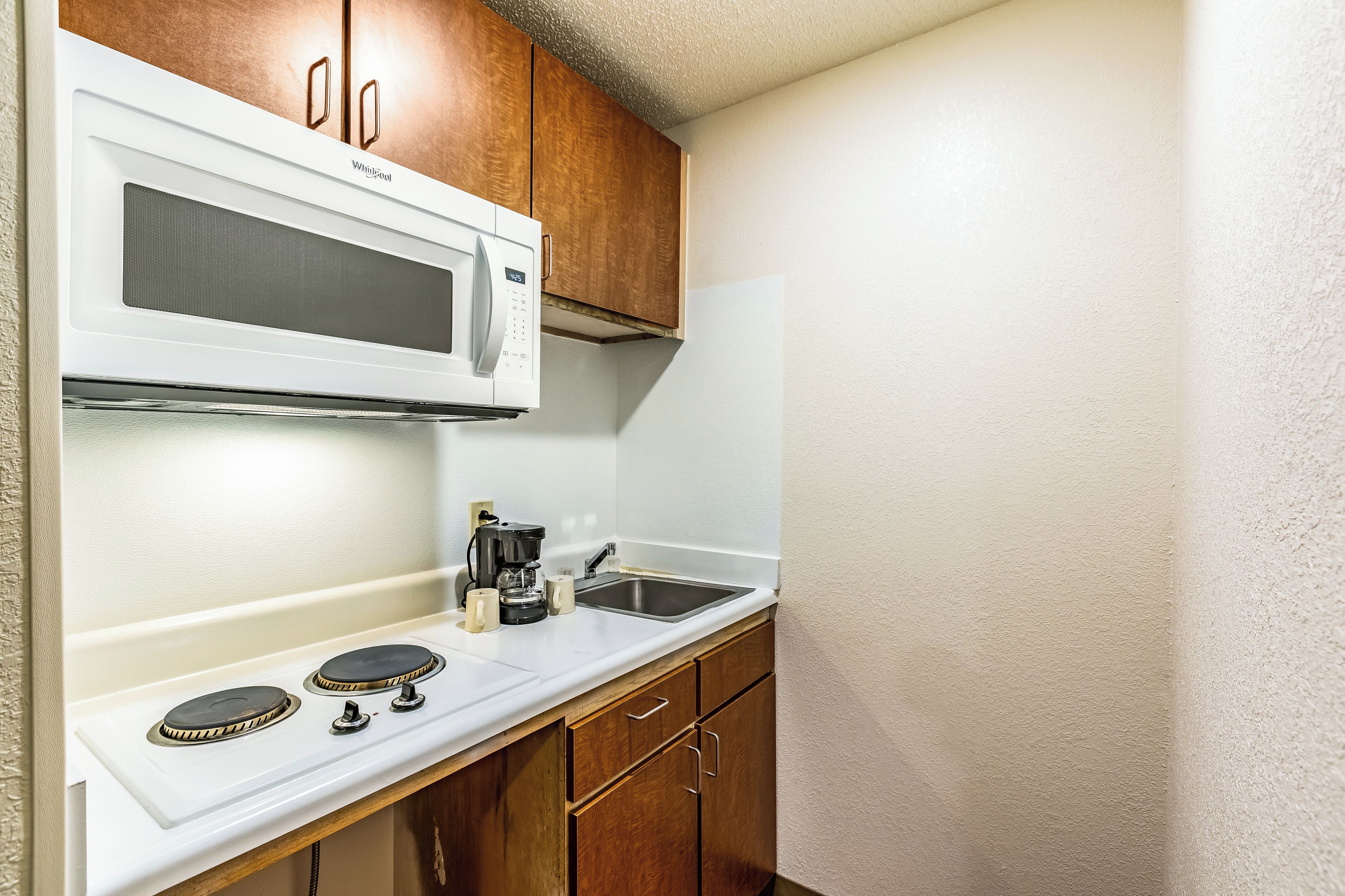 A compact kitchenette with a microwave, coffee maker, and a stove.