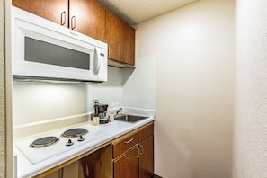 A compact kitchenette with a microwave, coffee maker, and a stove. - HomeTowne Studios by Red Roof Atlanta - Norcross Downtown (Norcross)